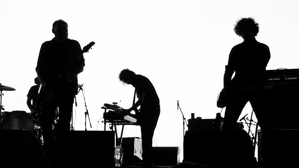 High contrast silhouette of a rock band performing live with musical instruments.