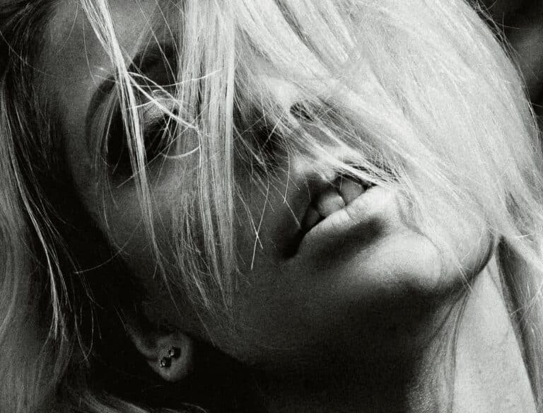 Dramatic black and white portrait of a woman with blonde hair and earrings, evoking a moody atmosphere.