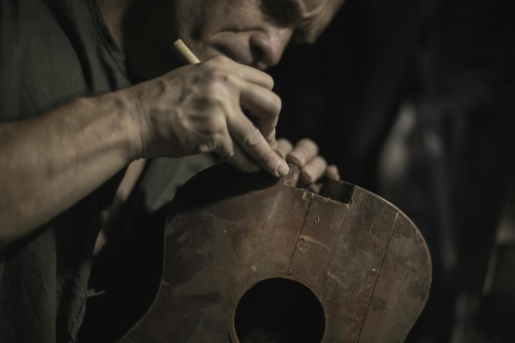 Close-up of a craftsman meticulously restoring an acoustic guitar in a workshop setting.