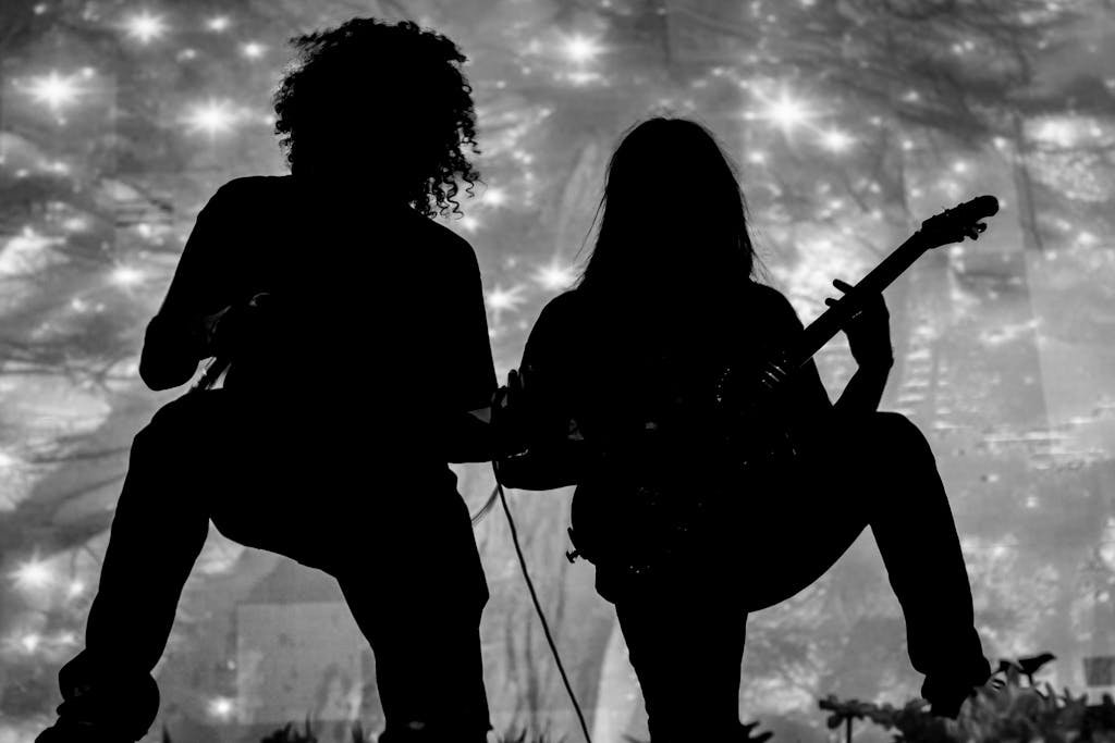 Silhouette of two musicians playing guitars against a vibrant background, conveying energy and passion.