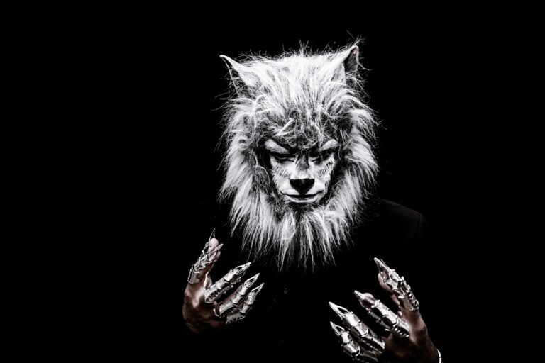 Striking portrait of an adult in a realistic werewolf costume with metallic claws against a black background.