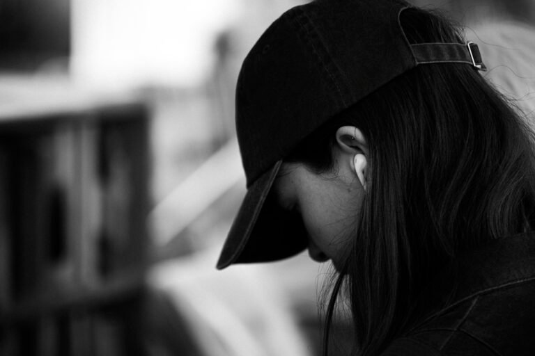 Artistic black-and-white portrait of a young woman wearing a cap and earbuds, exuding an urban lifestyle mood.