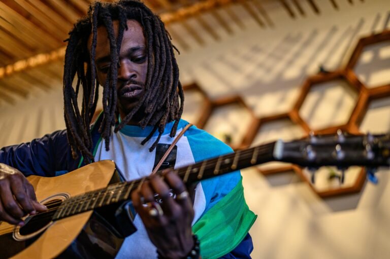 La Chitarra nel Reggae: Guida all'Ascolto attraverso i suoi Maestri 2 Close-up of a male musician playing an acoustic guitar during a performance indoors.