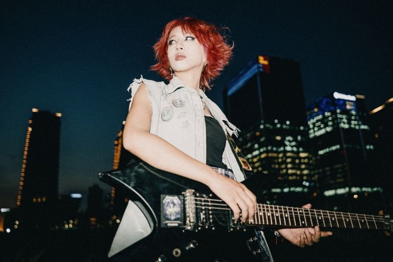 Donne e Chitarra: la Storia Nascosta dello Strumento più Amato del Rock 6 A woman with dyed hair plays an electric guitar against a city night skyline, showing urban rock vibes.