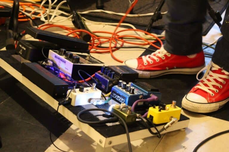 Close-up of a musician's pedal board adorned with colorful effects pedals and red sneakers.