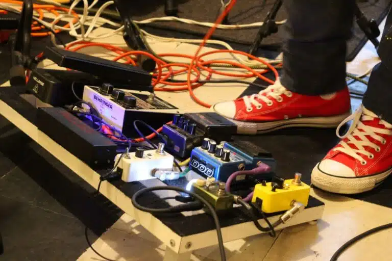 Chitarra e Tecnologia: come gli Effetti hanno Cambiato il Suono del Mondo 6 Close-up of a musician's pedal board adorned with colorful effects pedals and red sneakers.