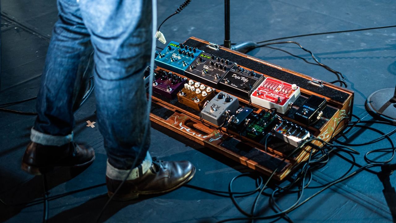 From above unrecognizable person in jeans standing on stage near pedalboard during music show