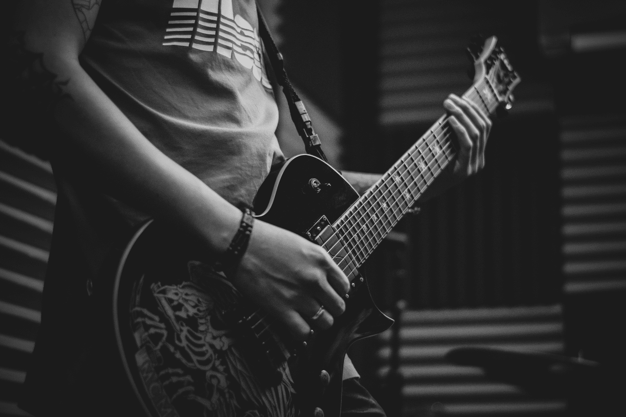 Monochrome photo of a guitarist playing electric guitar indoors.