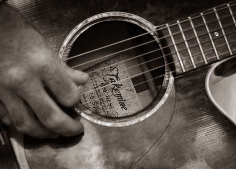 Sepia-toned close-up of a hand strumming an acoustic guitar, showcasing musical talent.