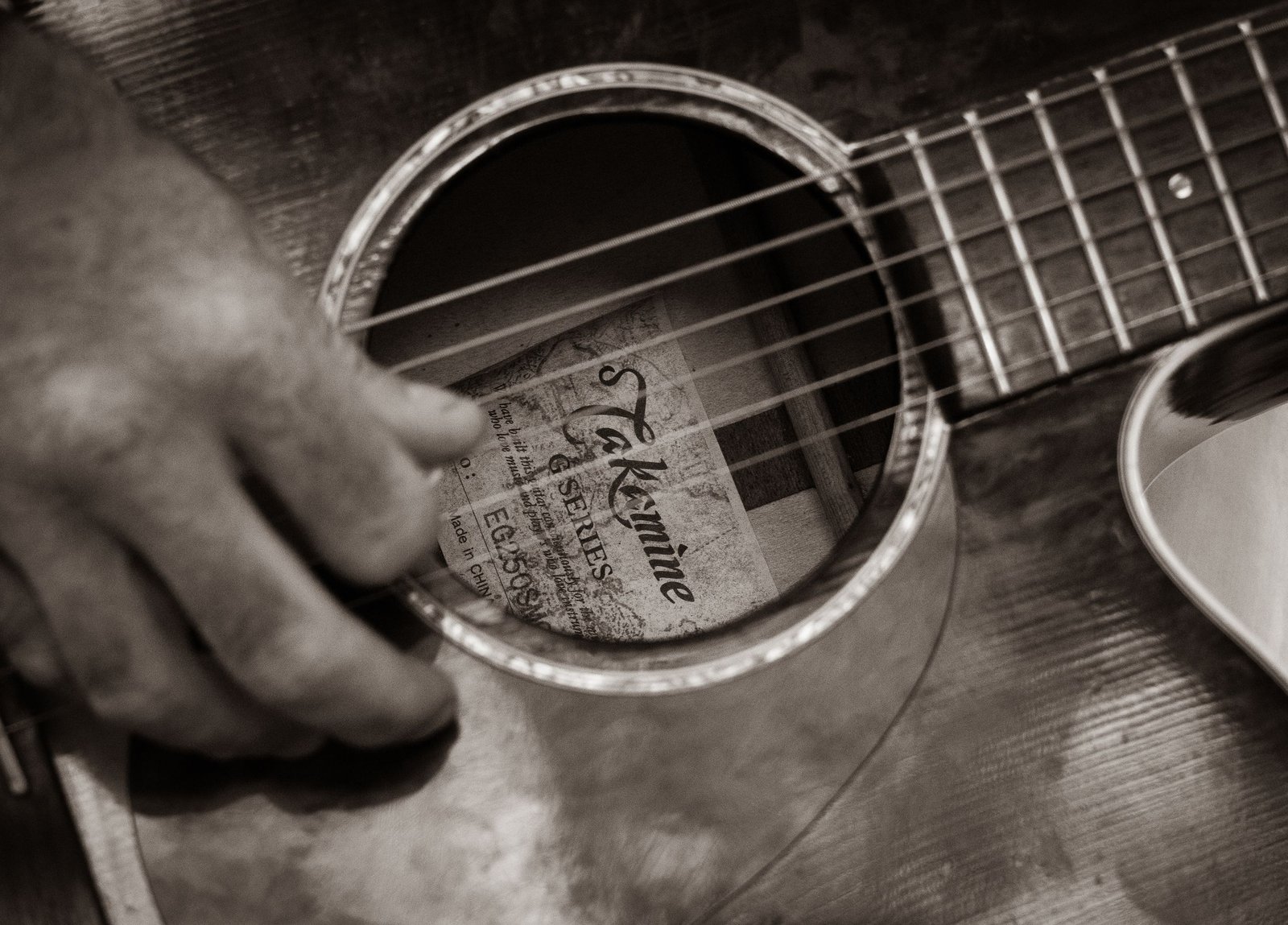 I 20 Migliori Chitarristi Italiani di Sempre: la Classifica Definitiva 1 Sepia-toned close-up of a hand strumming an acoustic guitar, showcasing musical talent.