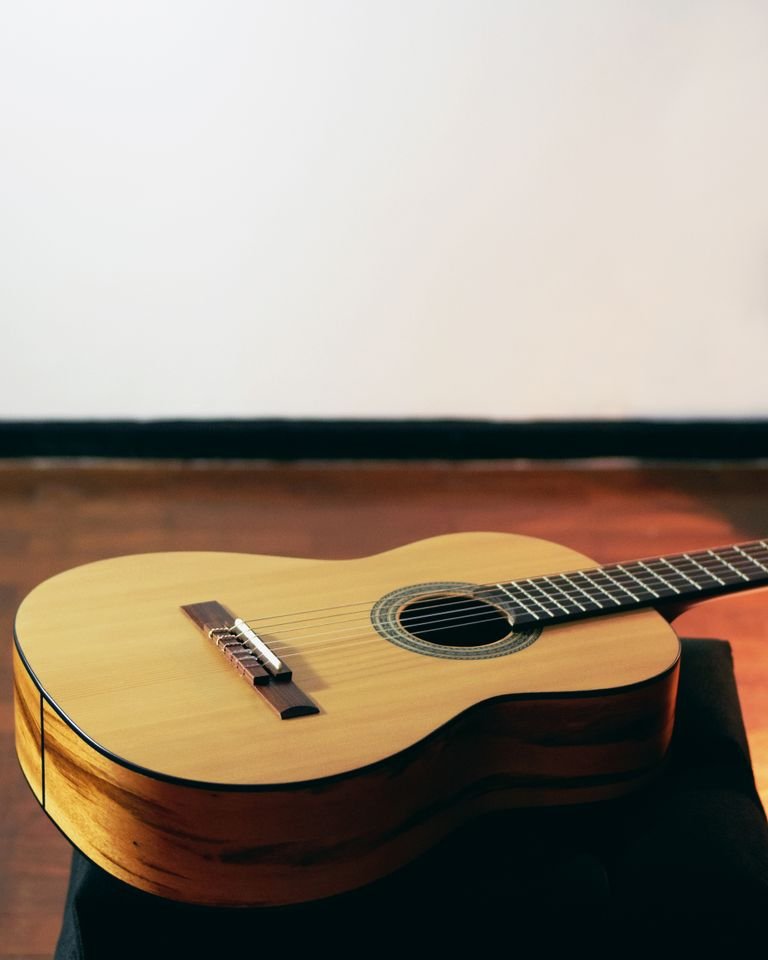Julian Bream e John Williams: i Maestri della Chitarra Classica del Novecento 1 Warm-toned acoustic guitar resting on a wooden floor with dramatic lighting.